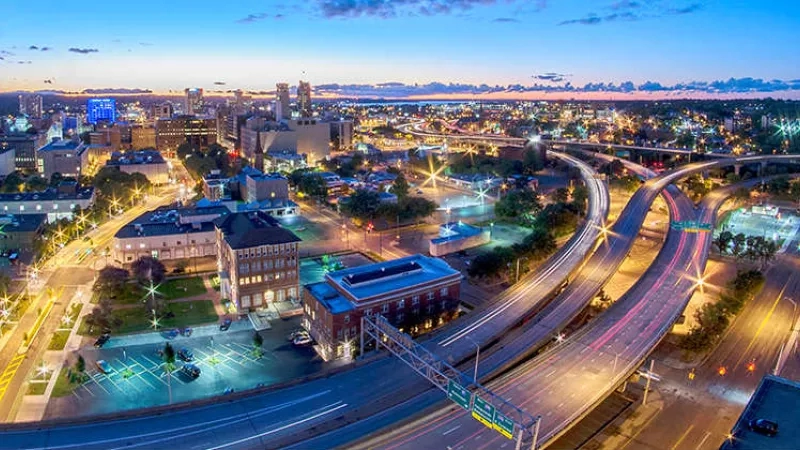 An aerial view of a city at dusk with buildings, roads, and a flyover in the foreground.