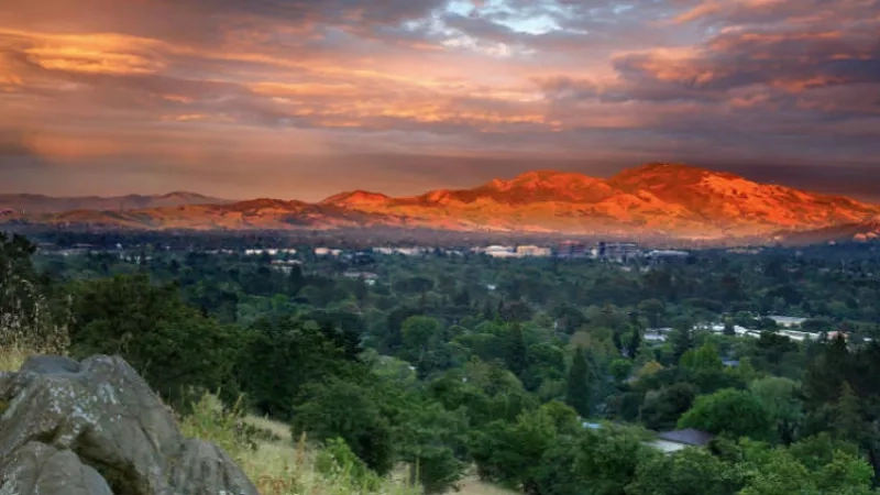 Sunrise over Berkeley Hills with a cityscape view of buildings and lush greenery under a vibrant sky.