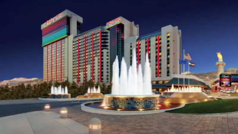 Atlantis Casino Resort Spa in Reno at night with lit-up buildings, fountains, flags, and mountains in the background.
