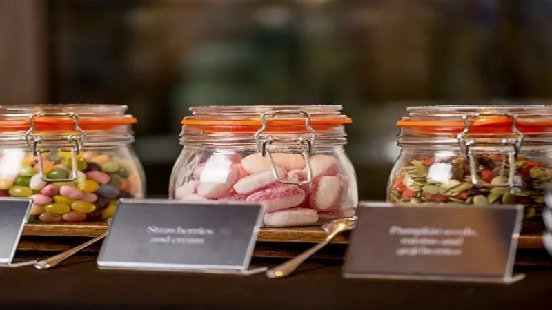 DDR conference food 4. Image of four jars with candy, seeds, and nuts with spoons and signs.