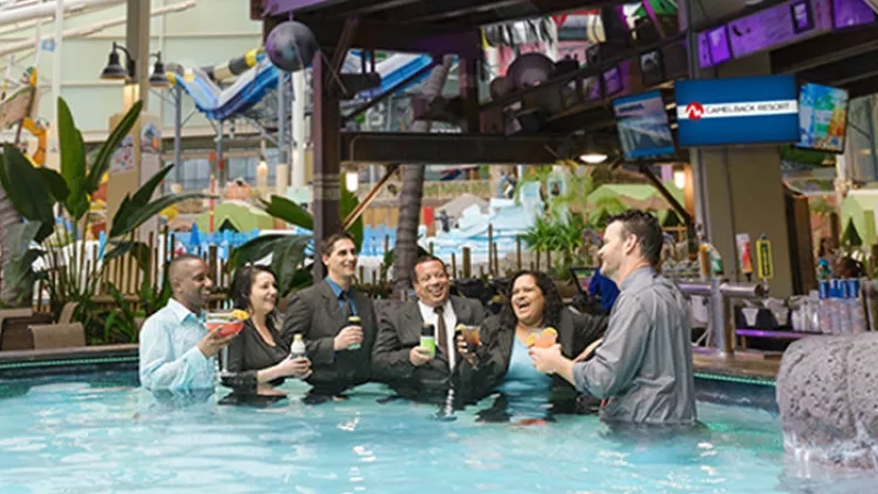 Group of people in water at a bar in an indoor waterpark with a slide in the background.