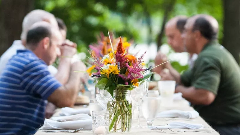 A group of men at a dinner table with a vase of flowers in the center.