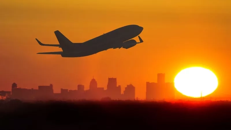 Airplane flying over a city at sunset with a warm orange and yellow sky.