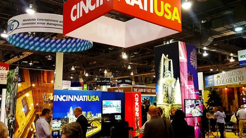 People walking around at a convention with Cincinnati USA and Destination Colorado banners hanging from the ceiling.