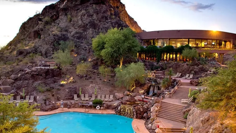 A hotel with a pool, mountain, stairs, and trees with a sunset view of the sky.