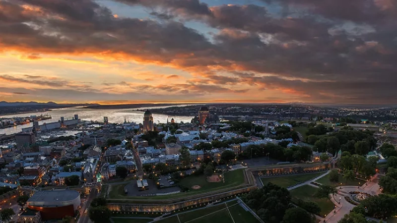 Quebec City with a city view, waterfront, and buildings at sunset, featuring a cloudy sky and trees.