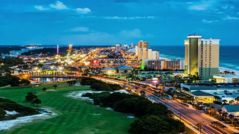 An aerial view of Panama City Beach at night, showing hotels, the ocean, and a golf course.