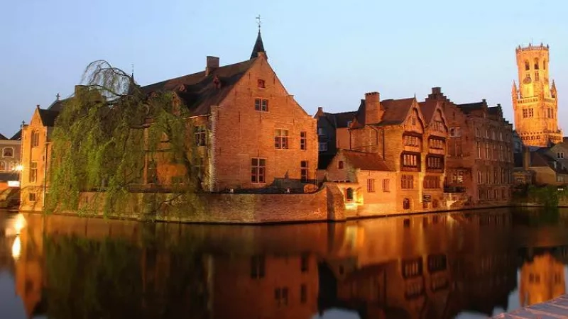 Bruges city at dusk, with the Belfry of Bruges and its reflection on a calm river.