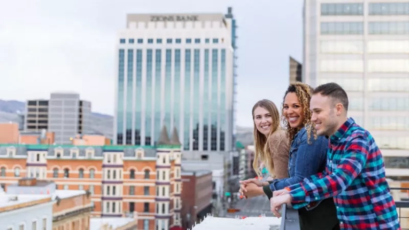 Three people stand on a balcony with the cityscape of Boise, Idaho, in the background.