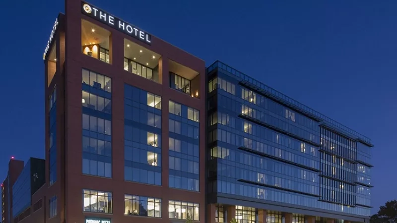 Exterior of the Hotel at night with lights on in the windows and trees in the background.