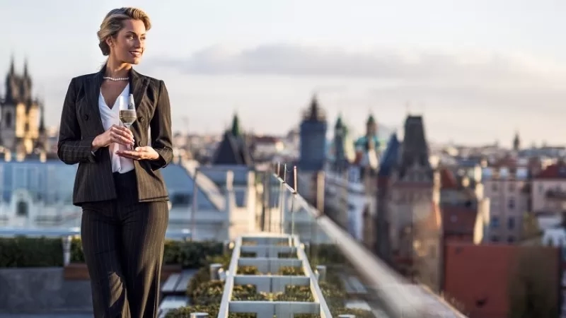 Woman with wine on rooftop terrace with city skyline in background, Four Seasons Hotel Prague.