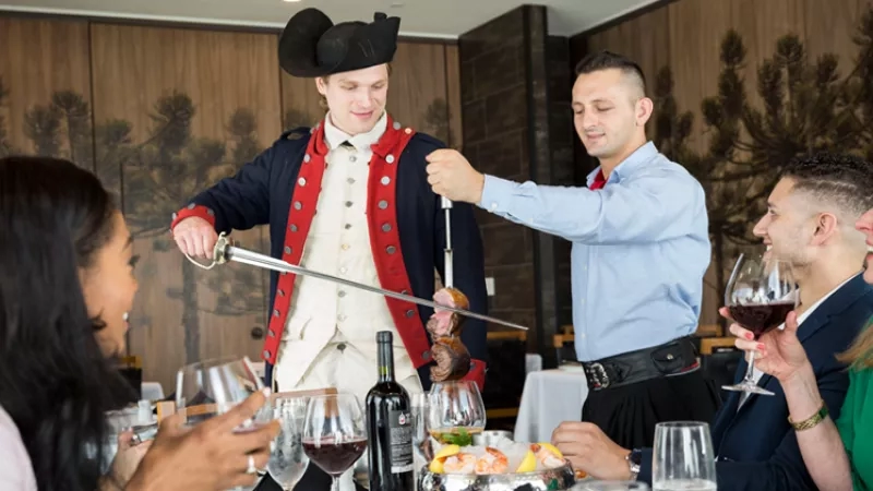 A group of people are sitting at a table, while a man is wearing a costume.