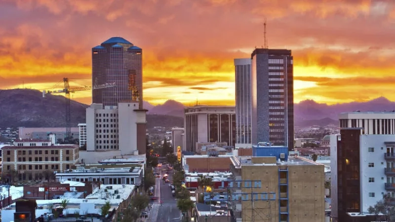 A cityscape of Tucson, Arizona, at sunset with a vibrant sky and prominent buildings.