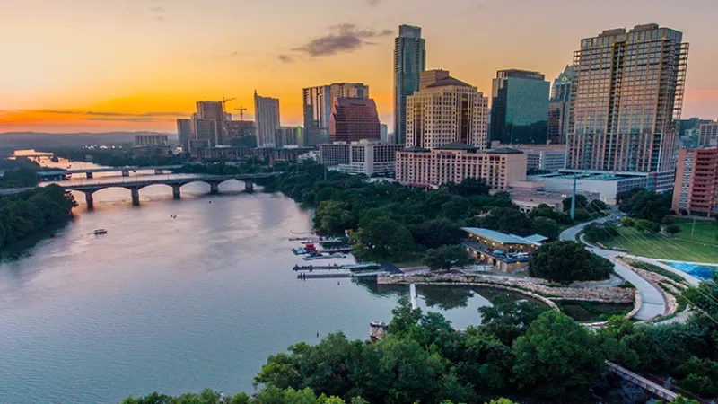Aerial view of Austin, Texas, at sunset with river, bridge, and cityscape.