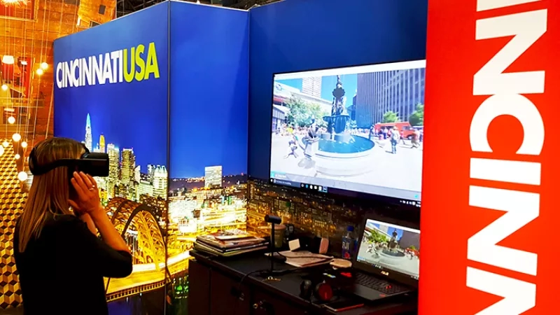 A woman wearing a virtual reality headset is exploring Cincinnati USA in front of a computer monitor.