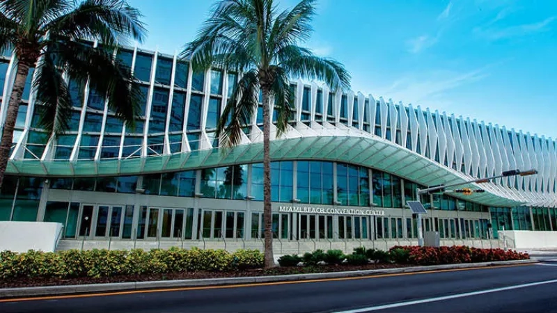 The Miami Beach Convention Center with glass facades, palm trees, and modern architecture in a sunny setting.