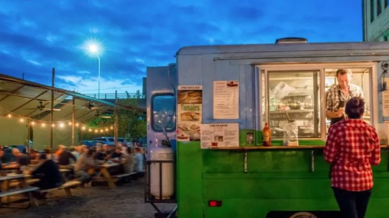 A man standing in the food truck and a woman in front of the food truck.