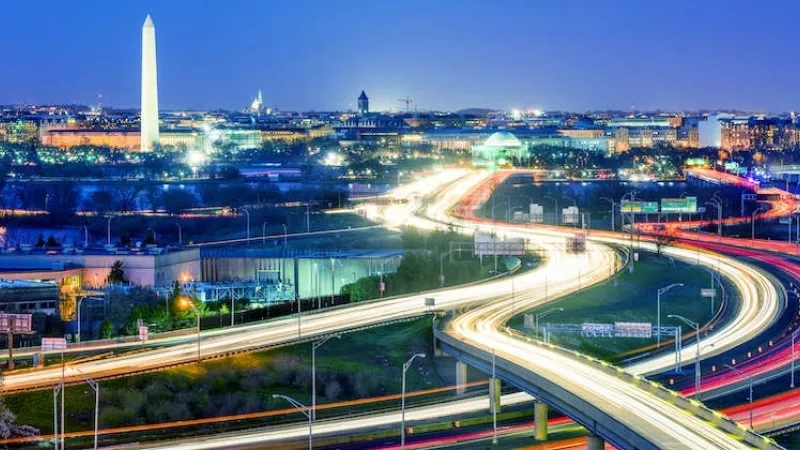 A night view of Washington, D.C., with the Washington Monument in the background and a highway below.