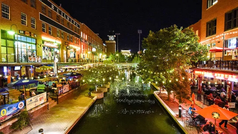 A night view of San Antonio River Walk with a river, buildings, trees, and people dining.