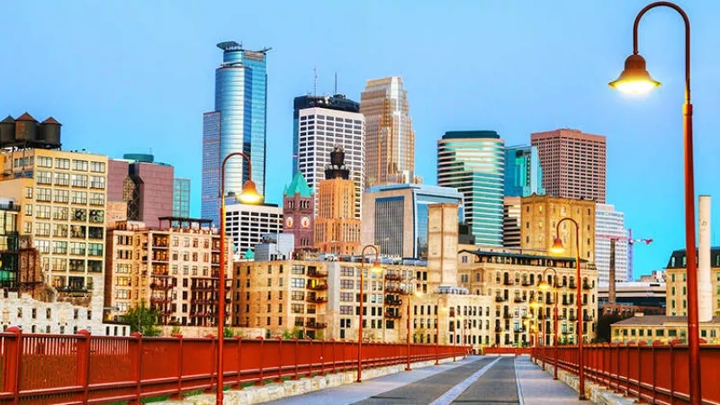 A red bridge leads to the city of Minneapolis, Minnesota, USA, with tall buildings in the distance.