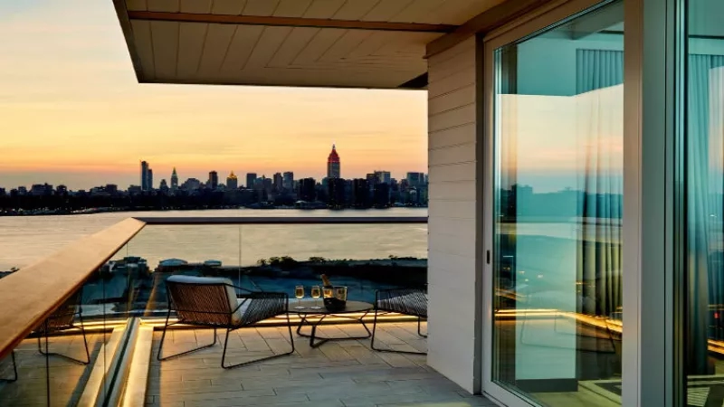 Balcony with chairs, table, and stunning city skyline view at sunset in an architecturally designed home.