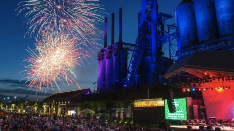 A crowd of people enjoying a fireworks display in front of a large steel building at night.