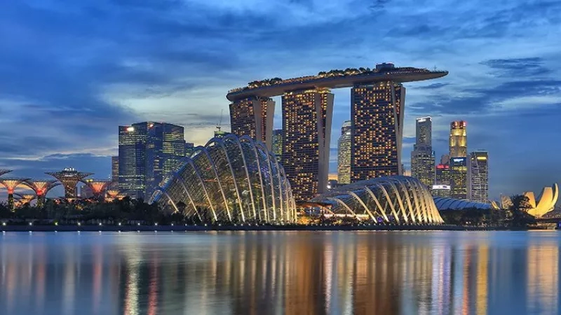 Singapore city skyline with Gardens by the Bay and Marina Bay Sands at dusk with reflection on the water.