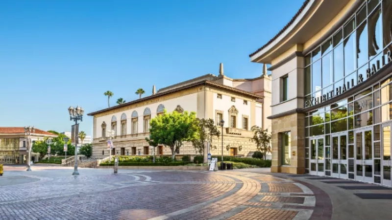 Pasadena Civic Center building with lush trees, brick pavement, and a blue sky on a sunny day.