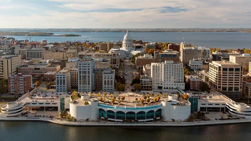 Aerial view of the Madison cityscape featuring modern architecture, greenery, and a serene water body.
