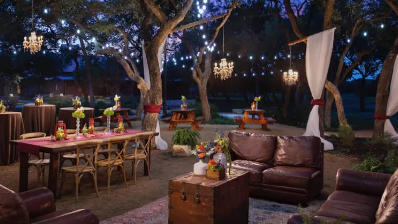 The Henry's Hollow glamping event features a dining area with tables, chairs, and chandeliers in a serene outdoor setting.