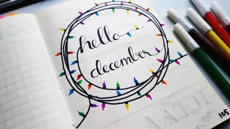 A notebook with the words "Hello December" written in string lights with colored markers on the side.