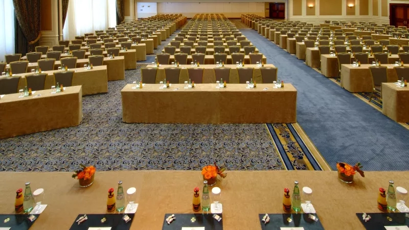 The Hotel Palace Berlin conference room has tables, chairs, a carpet, and paper with pens on it.