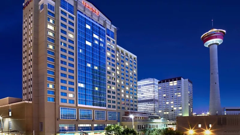 Exterior of Hyatt Regency Calgary at night with Calgary Tower in the background.