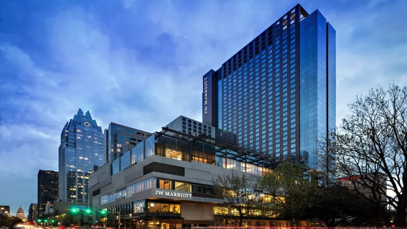Exterior view of JW Marriott Austin building at dusk with a cityscape in the background.