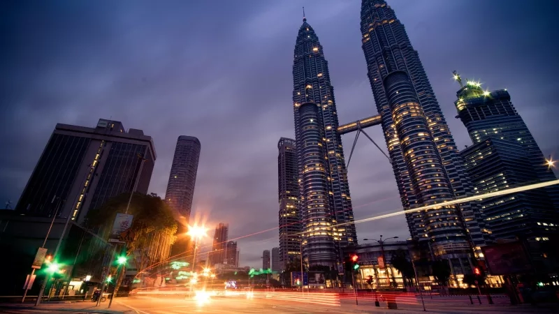 A cityscape of Kuala Lumpur with the Twin Petronas Towers in the background and traffic lights.