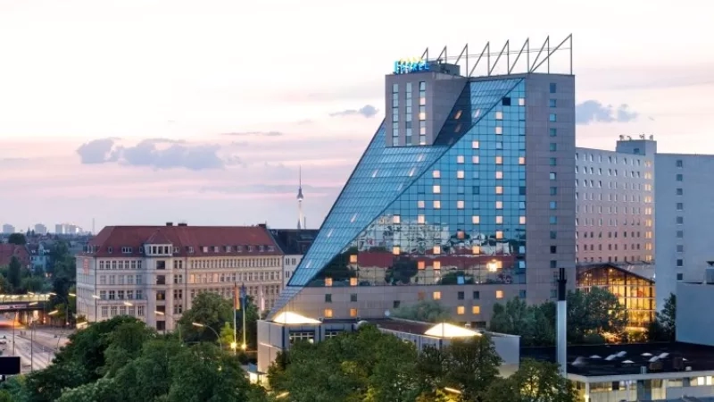 The Estrel Berlin hotel exterior features modern architecture, glass facades, and lush landscaping.