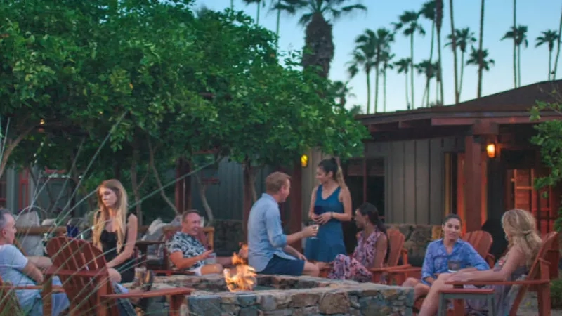 A group of people sitting around a fire pit in the evening at The Parker Palm Springs.