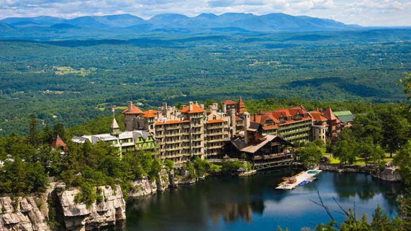 Aerial view of Mohonk Mountain House, with lake and lush greenery, and distant mountain range.