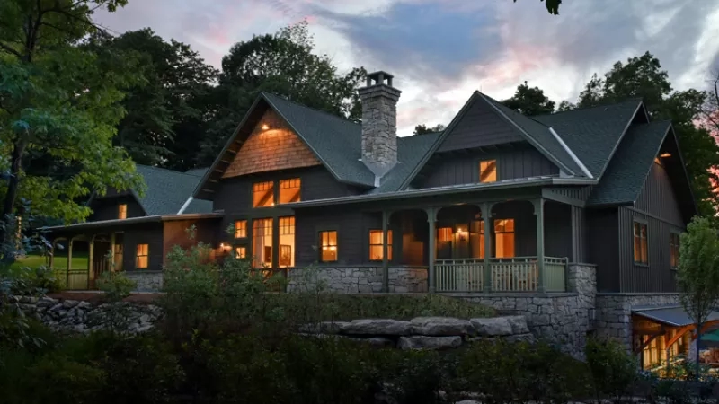 Exterior of a Mohonk Lake house at sunset with trees, bushes, and a stone walkway.