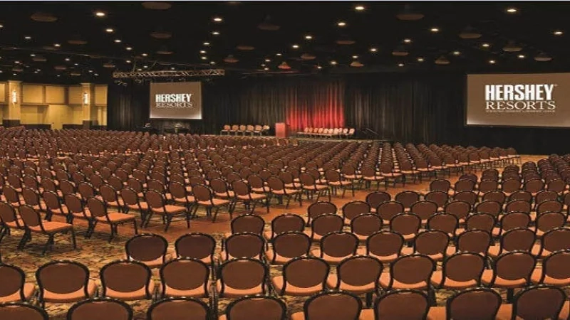 An empty conference room at Hershey Resorts with rows of chairs and a large screen on the wall.