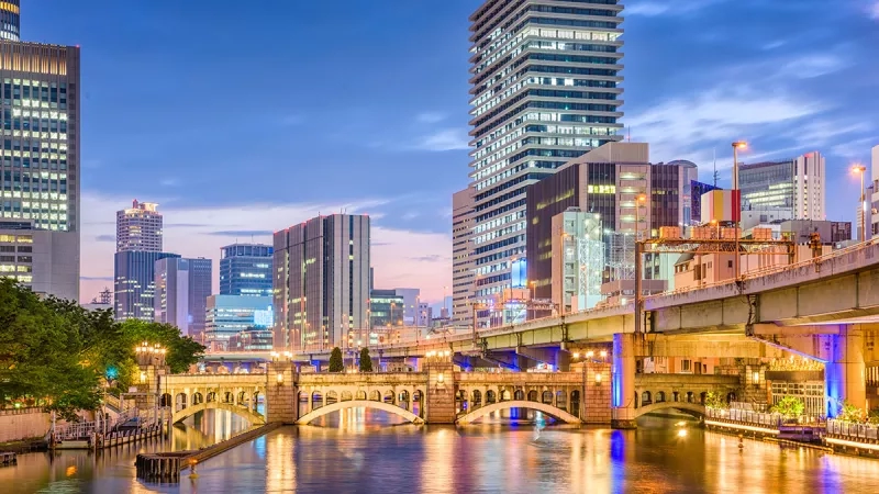 Osaka Japan with a river and a bridge with an overpass and buildings on a dusk.