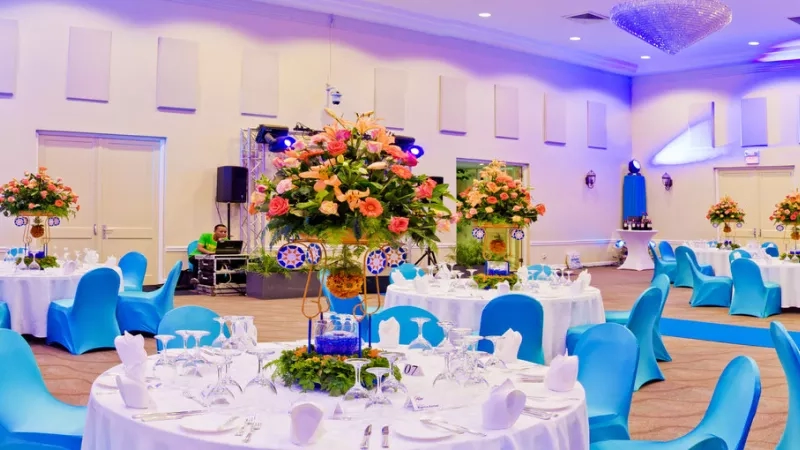 A large hall of Royal Torarica has many tables and chairs, and it is decorated with lights and flowers.