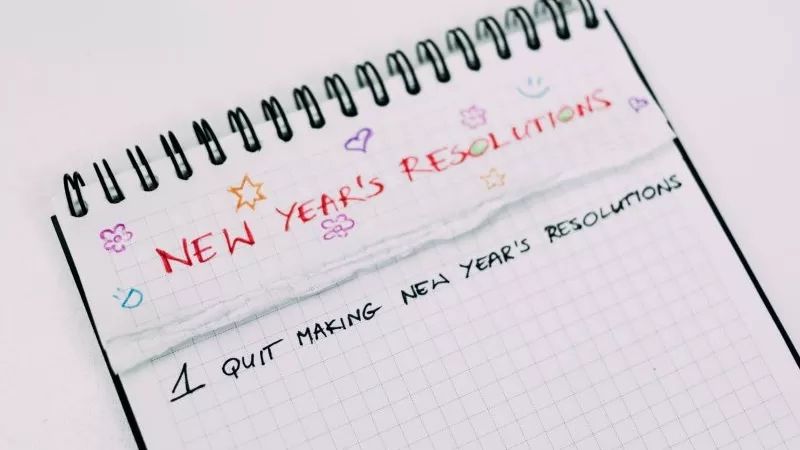 A torn piece of paper with "New Year's Resolutions" written on it is taped to a notepad.
