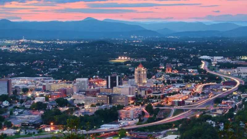 A city skyline with a backdrop of mountains, illuminated by the soft glow of dusk or dawn.
