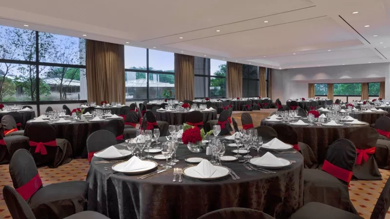 A view of a banquet hall with black tables and chairs and red ribbons in Sheraton Buenos Aires.