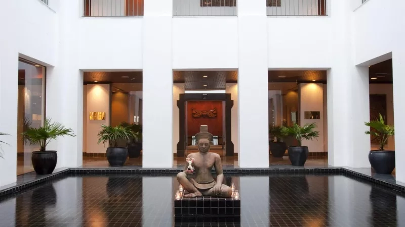 Sukothai: A serene, modern building with a statue, black tiles, and lush potted plants.