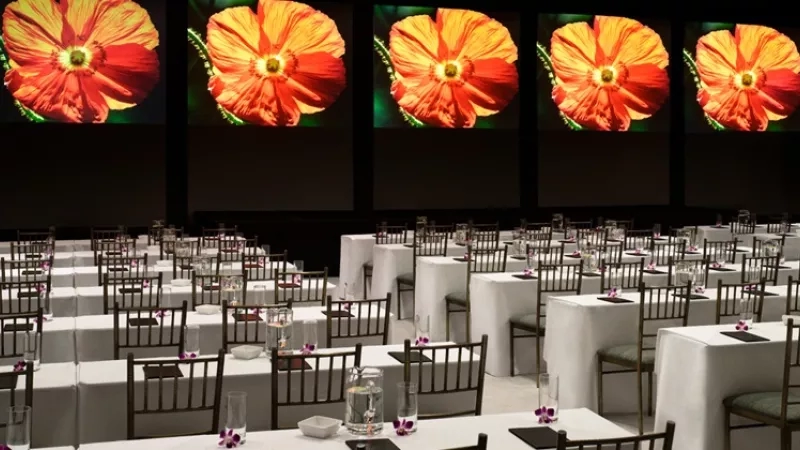 A banquet hall with large screens displaying orange flowers and rows of tables and chairs.