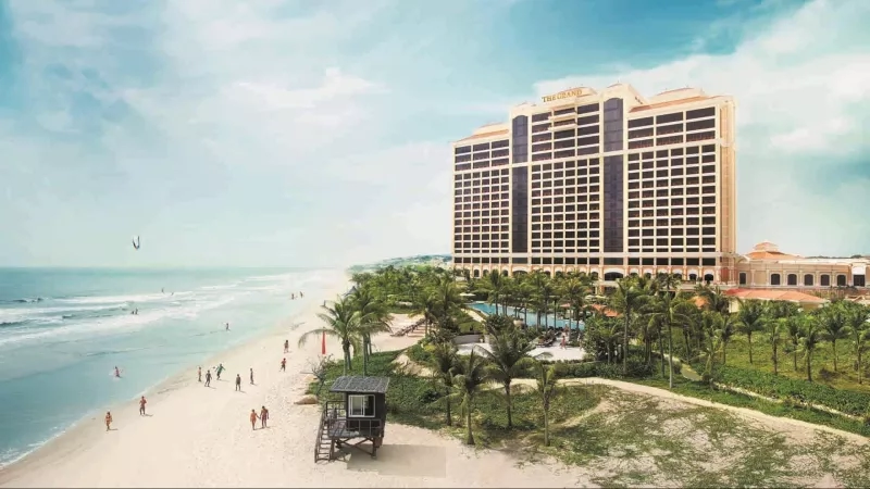 Beach view of The Grand Ho Tram Strip hotel in Vietnam with lush landscaping and people enjoying.