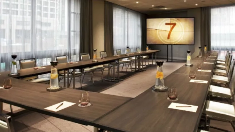 An empty meeting room with chairs, a long table, and a projector screen with a number "7" on it.