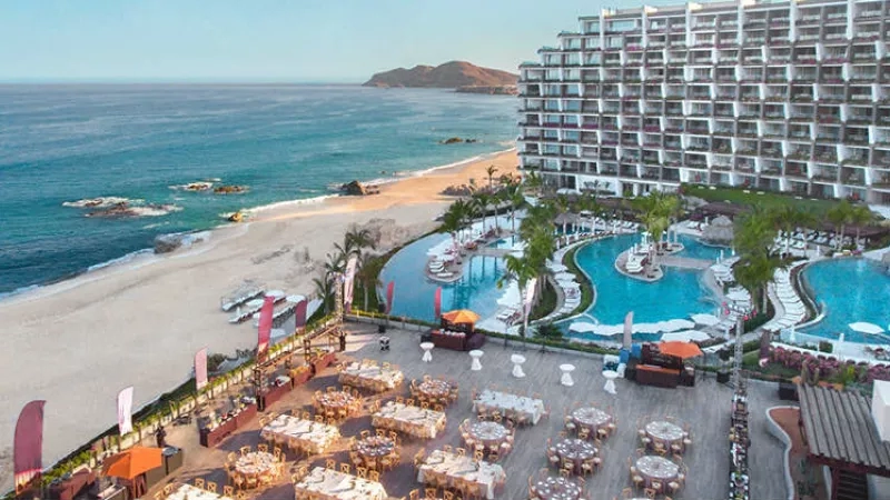 An aerial view of a resort with a large building, a beach, and a pool.